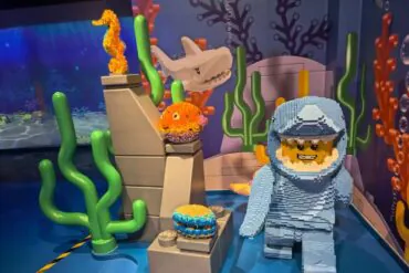 LEGO undersea display with a brick-built diver in blue, a white shark head, orange sea creatures, and green coral shapes.