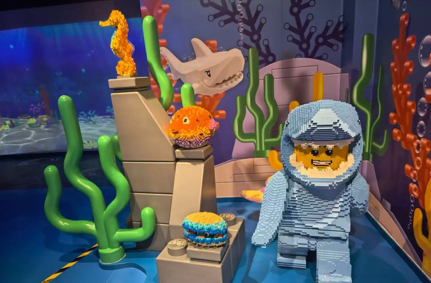 LEGO undersea display with a brick-built diver in blue, a white shark head, orange sea creatures, and green coral shapes.