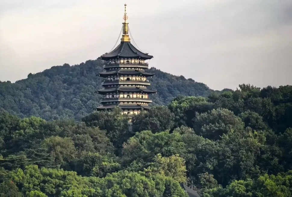 Leifeng Pagoda,Hangzhou,Chinatour Seven-story pagoda perched among green trees on a hillside in a forested landscape, with a cloudy sky above.