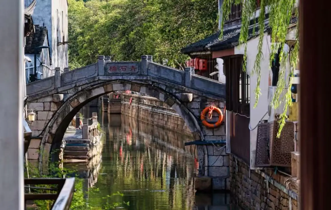 Pingjiang Road Historical Street,Suzhou,Chinatour Stone arch bridge over a narrow canal in a traditional Chinese water town, with green trees and lanterns nearby.