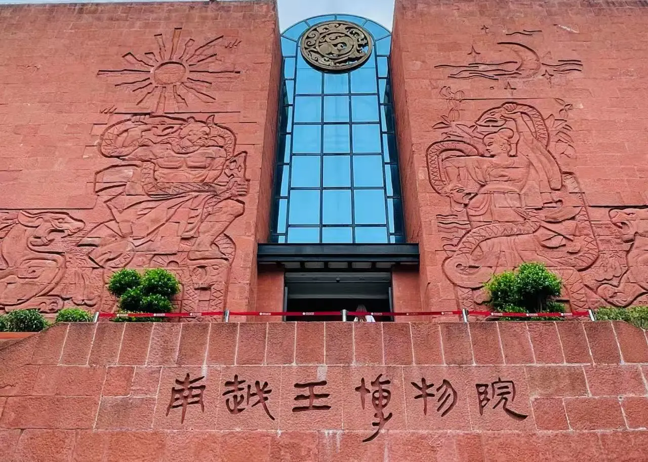 Museum of the Mausoleum of the Nanyue King,Guangzhou,Chinatour Front view of a red brick museum facade featuring large stone reliefs on both sides, a blue glass central tower, and Chinese characters along the lower wall.