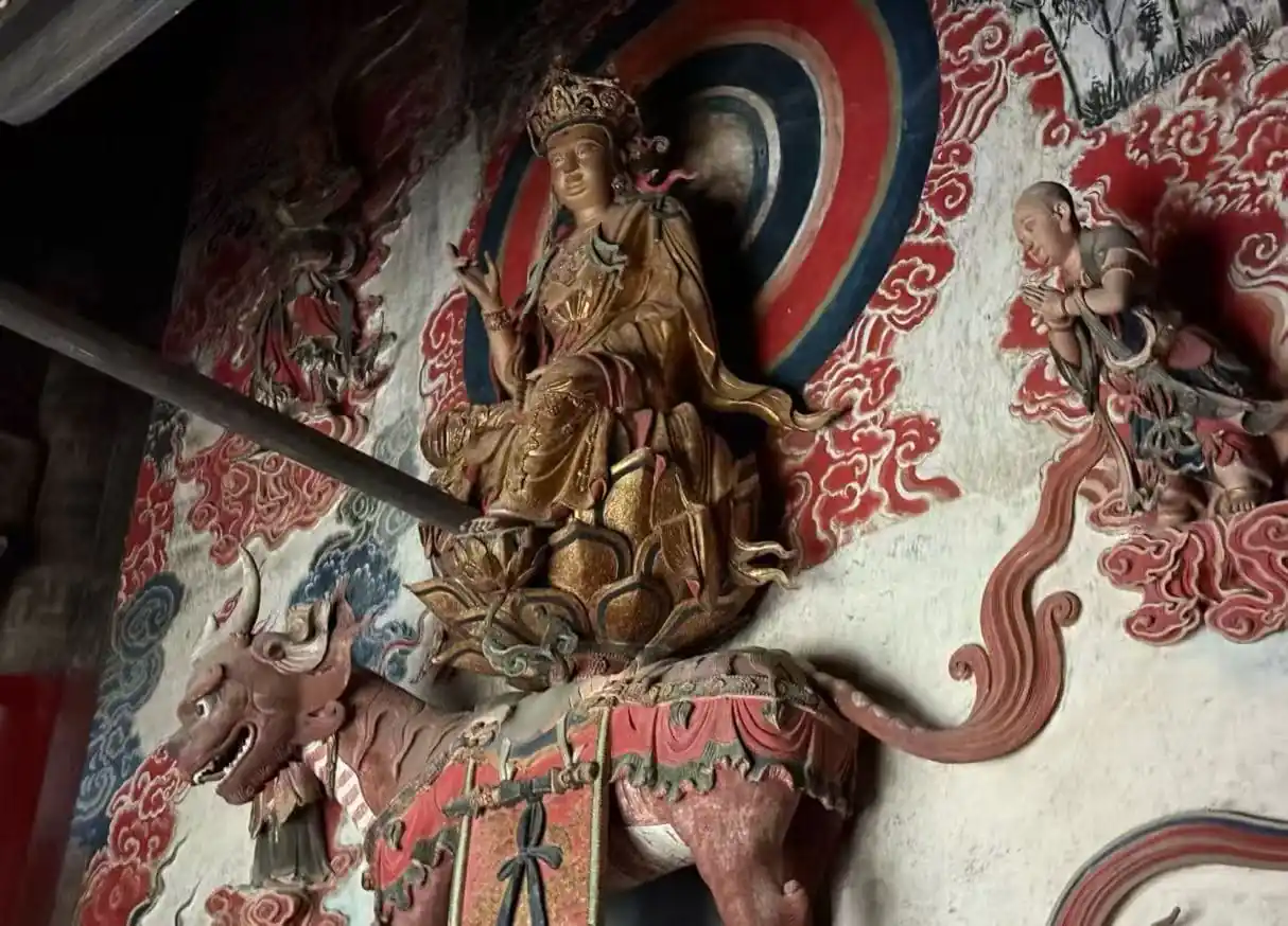 Golden crowned deity seated on a dragon, mounted on a richly painted temple wall backdrop of red cloud motifs.
