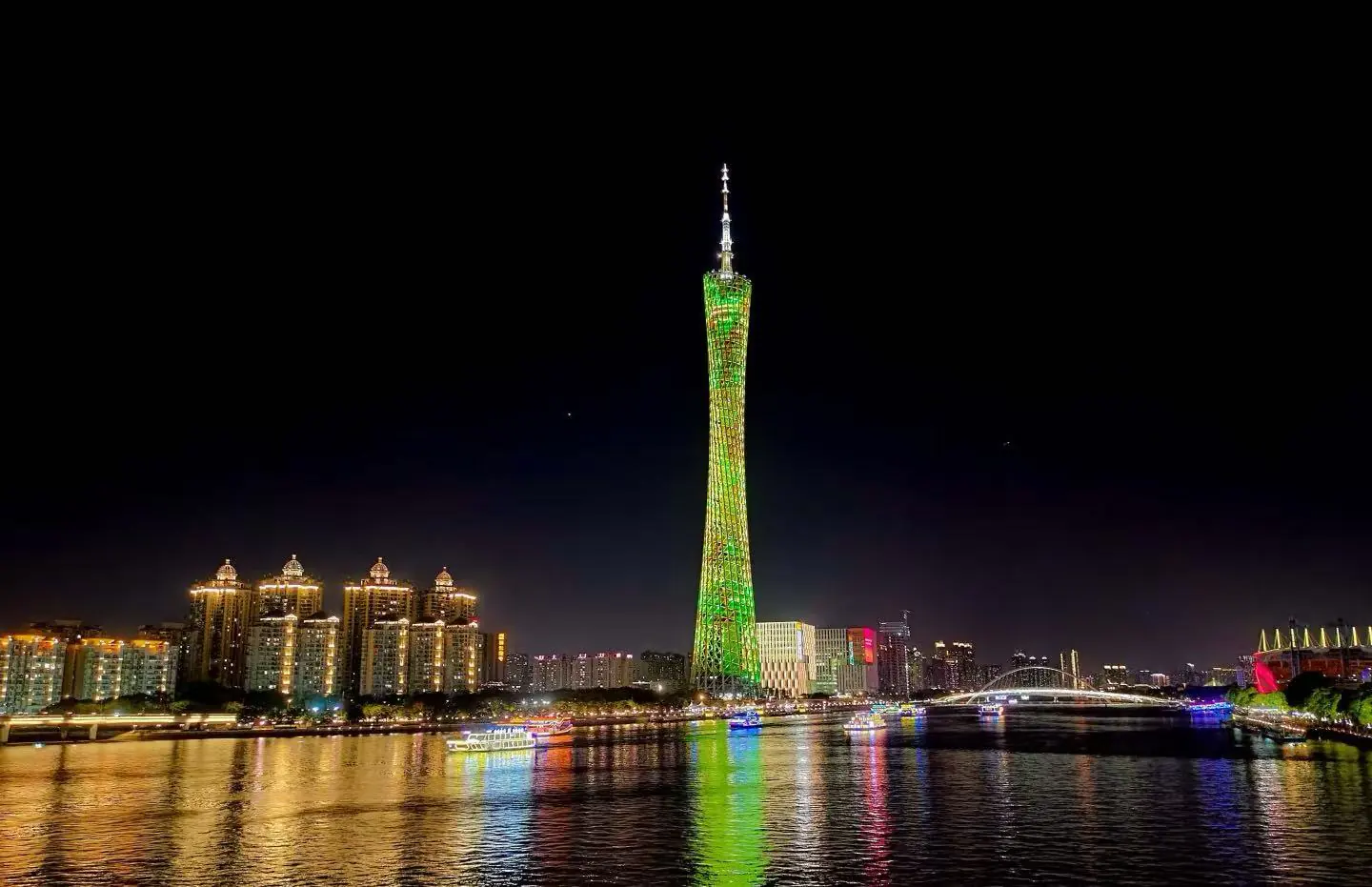 Guangzhou Pearl River Night ,Guangzhou,Chinatour Guangzhou Canton Tower lit green at night beside a riverfront city skyline with reflections on the water, illuminated buildings in the background.