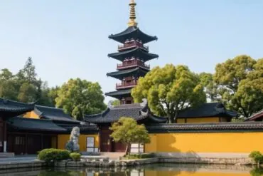 Five‑tier pagoda with a gold finial rises above yellow temple walls, surrounded by trees and a tranquil pond reflection.