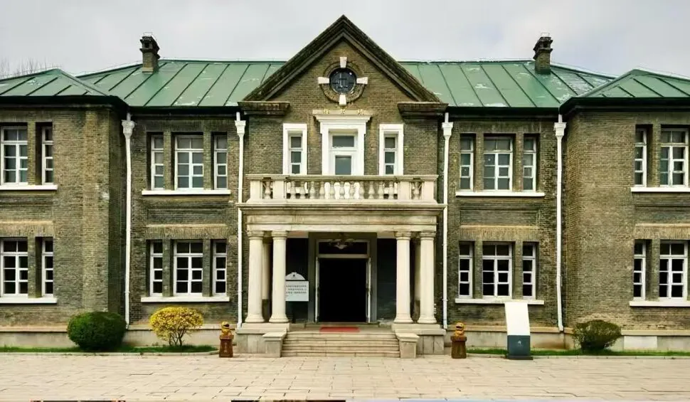 Historic brick building with a central columned portico, balcony, and a clock at the gable. Symmetrical wings flank the entrance.