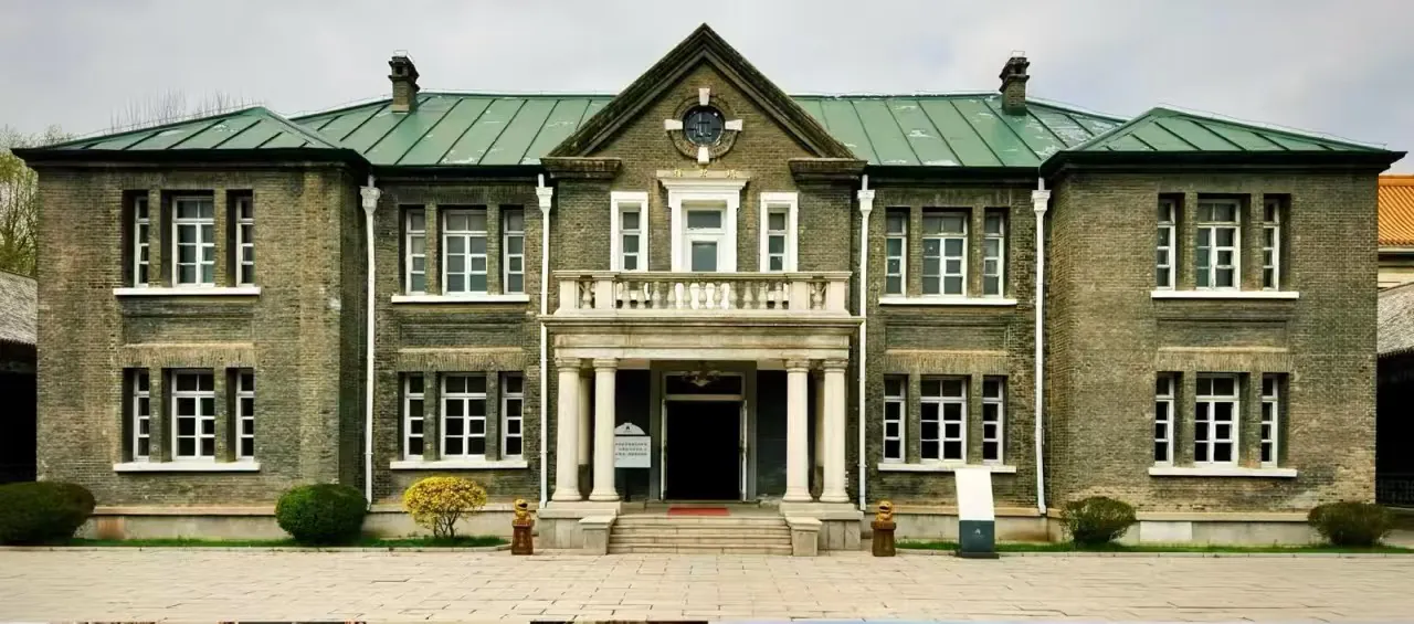Manchu State Imperial Palace Museum,Changchun,Chinatour Historic brick building with a central columned portico, balcony, and a clock at the gable. Symmetrical wings flank the entrance.