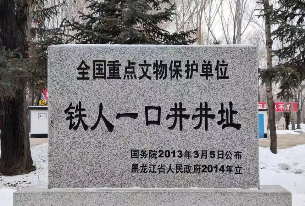 Granite stele with Chinese inscription declaring a national key cultural relic protection site, set in a snowy park with trees in the background.