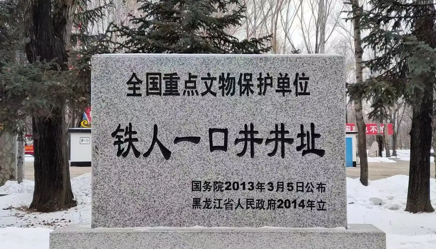 Granite stele with Chinese inscription declaring a national key cultural relic protection site, set in a snowy park with trees in the background.