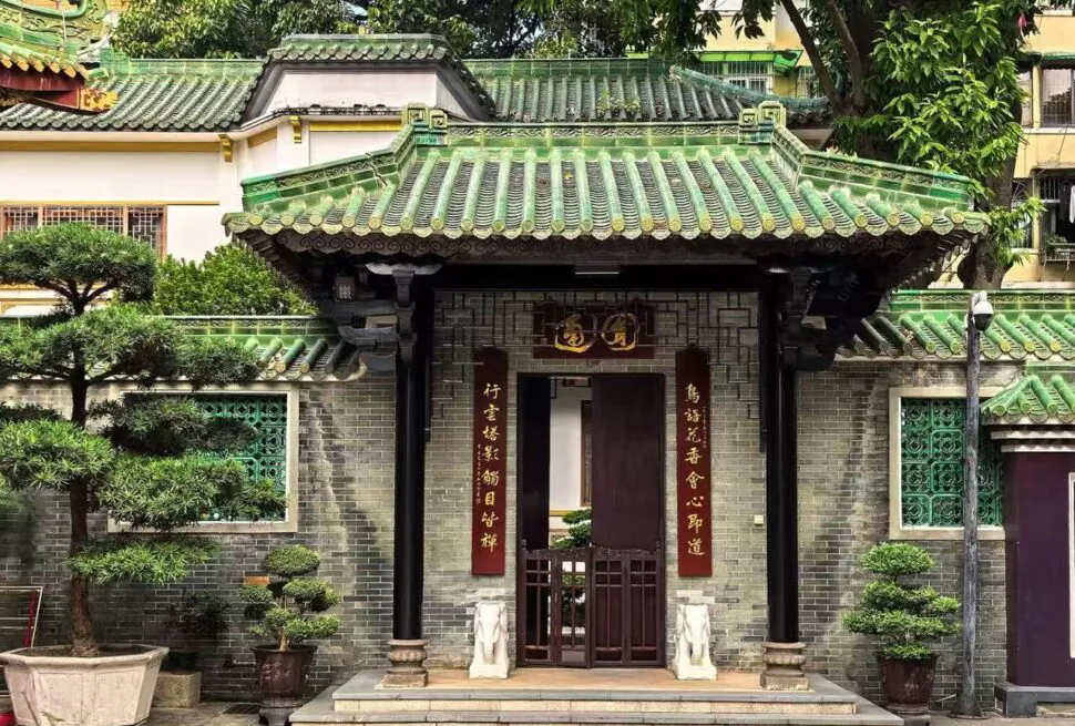 Temple of the Six Banyan Trees,Guangzhou,Chinatour Traditional Chinese gate with a green tiled roof and red couplets, opening to a small courtyard garden.