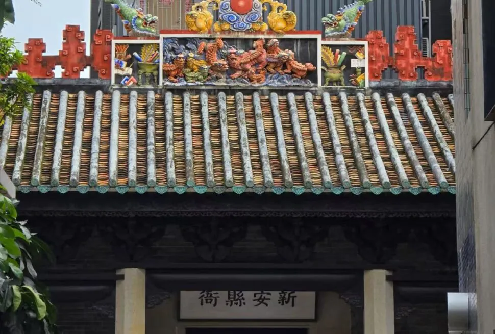 Colorful traditional temple roof with ceramic dragon statues and ornate tiles above a dark doorway and Chinese plaque beneath.