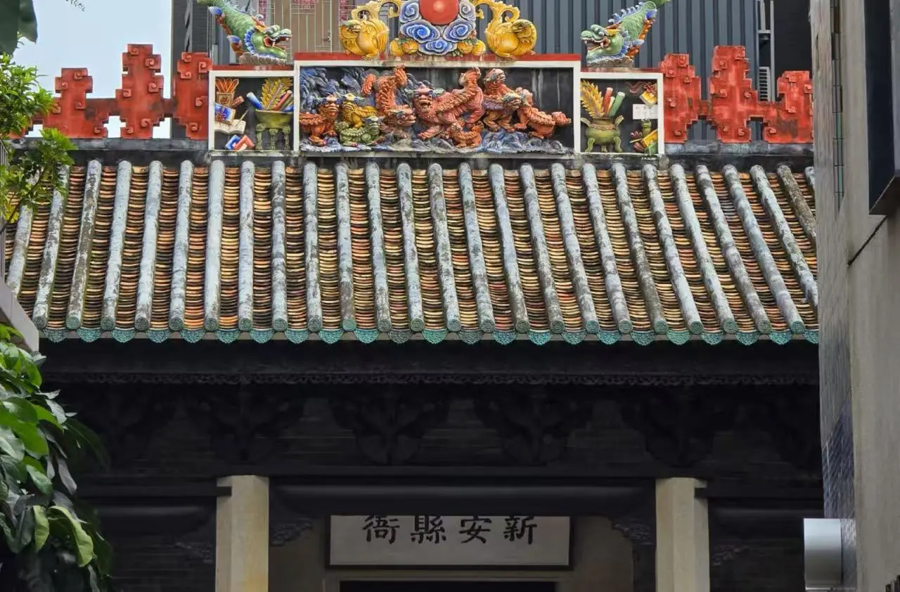 Colorful traditional temple roof with ceramic dragon statues and ornate tiles above a dark doorway and Chinese plaque beneath.