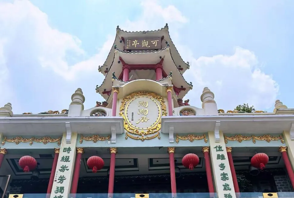 Front view of a Chinese temple with red columns, gold ornamentation, and red lanterns against a blue sky.