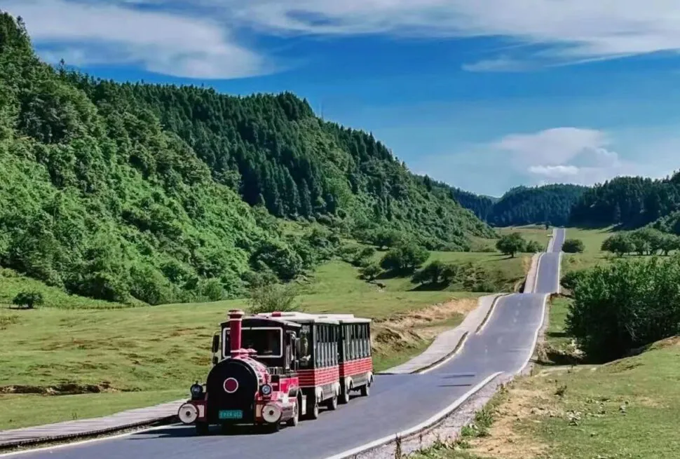 Nanshan Scenic Area,Chongqing,Chinatour A red-and-black tourist train traveling on a winding rural road through green hills and forests under a blue sky.