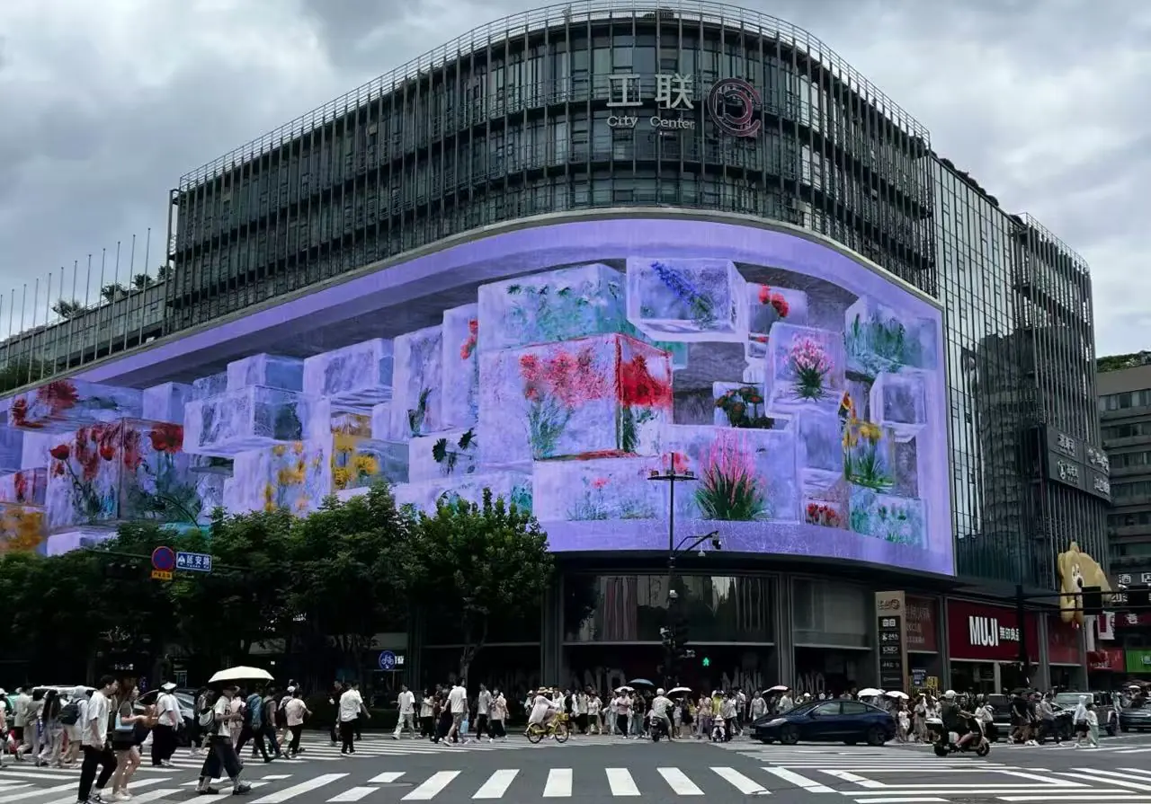 Hubin Shopping District ,Hangzhou,Chinatour Busy city street scene with a curved LED screen on a glass-fronted building displaying colorful flower images as pedestrians cross the crosswalk.