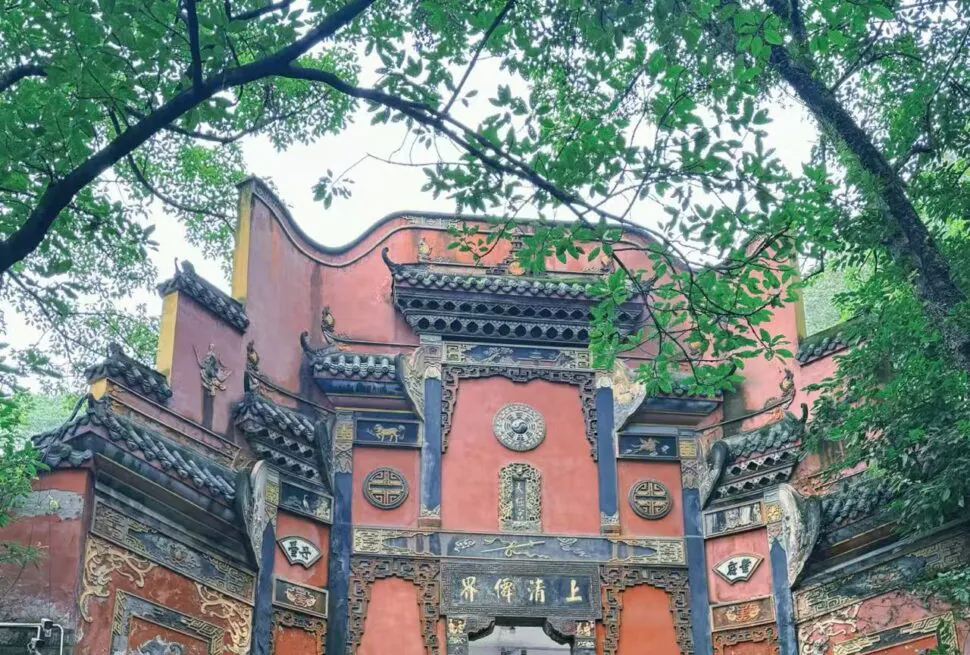 Ornate red Chinese temple gate with blue-gray decorative panels and gold carvings, framed by green trees.