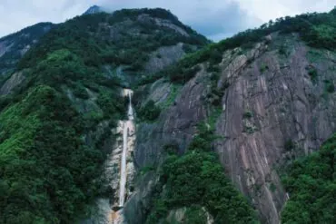 Forested mountain with a thin waterfall cascading down a rocky crevice between steep cliffs.