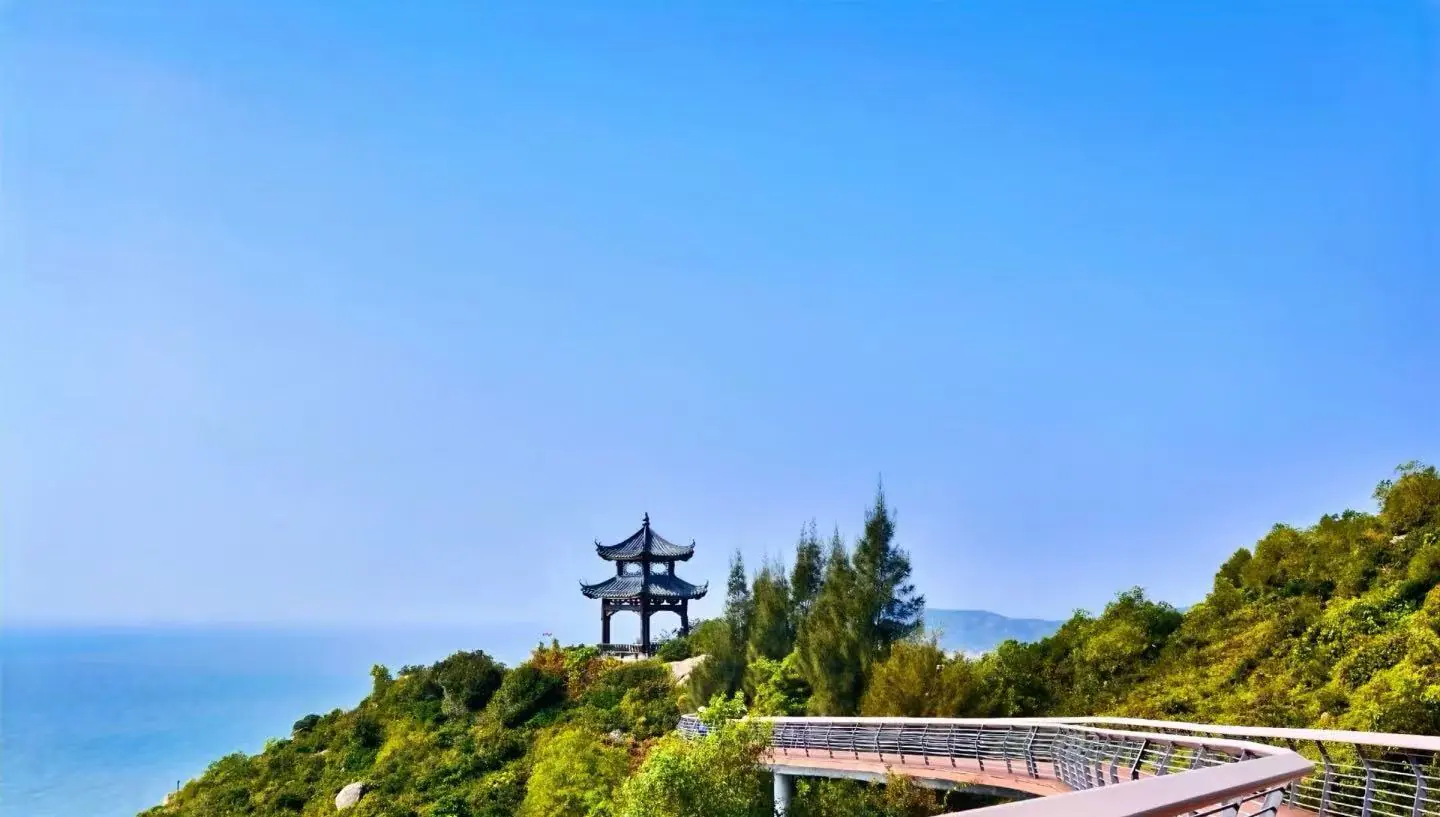 Zhuhai Islands,Zhuhai,Chinatour Traditional pagoda on a hillside overlooking a blue sea, with a curved wooden boardwalk in the foreground.