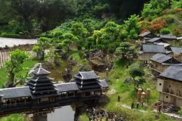 Miniature traditional Asian village with tiered pagoda buildings, a wooden bridge, and lush garden scenery.