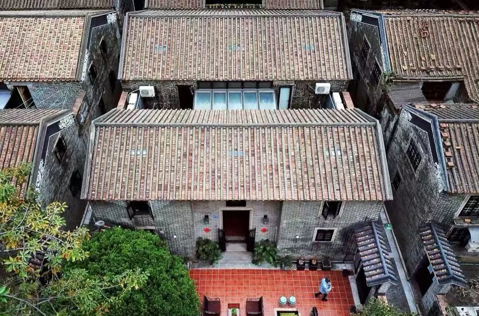 Aerial view of grey brick houses with tiled roofs forming a narrow courtyard, red tile courtyard in front of a central doorway with a person nearby.