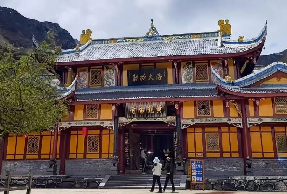 Front view of a colorful traditional Chinese temple with ornate roof decorations and yellow walls, set against rocky mountains. (Informative)
