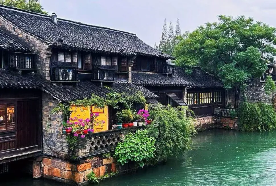 Canal-side stone houses with tiled roofs and hanging balconies, colorful flowers in pots along the wall.