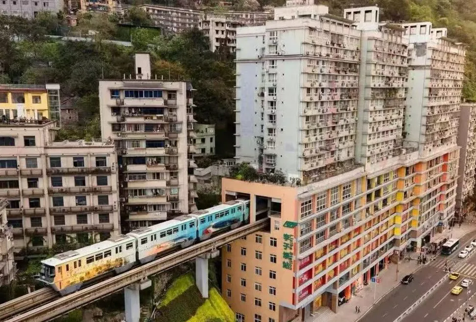 Elevated metro train passing between colorful high-rise buildings on a hillside city street.