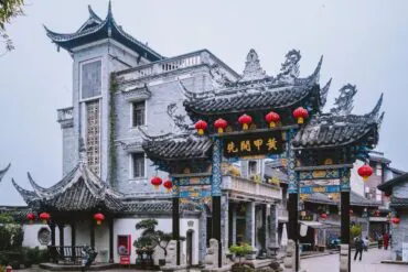 Ornate Chinese paifang arch with blue-gold detailing and red lanterns in a temple courtyard