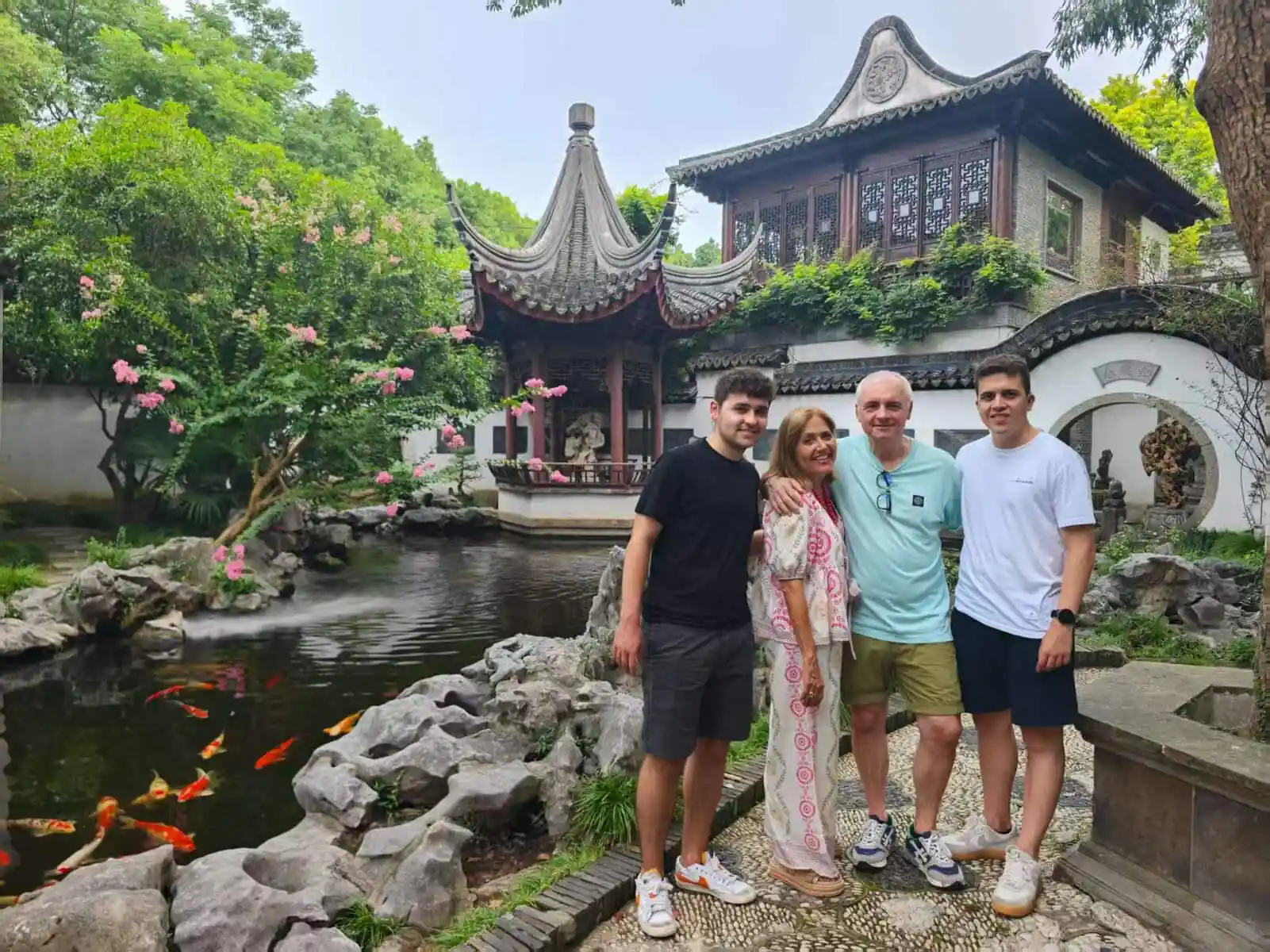 CET traveler story - Spanish family,Chinatour Four people pose together in a traditional Chinese garden with koi pond and a curved pavilion behind them.