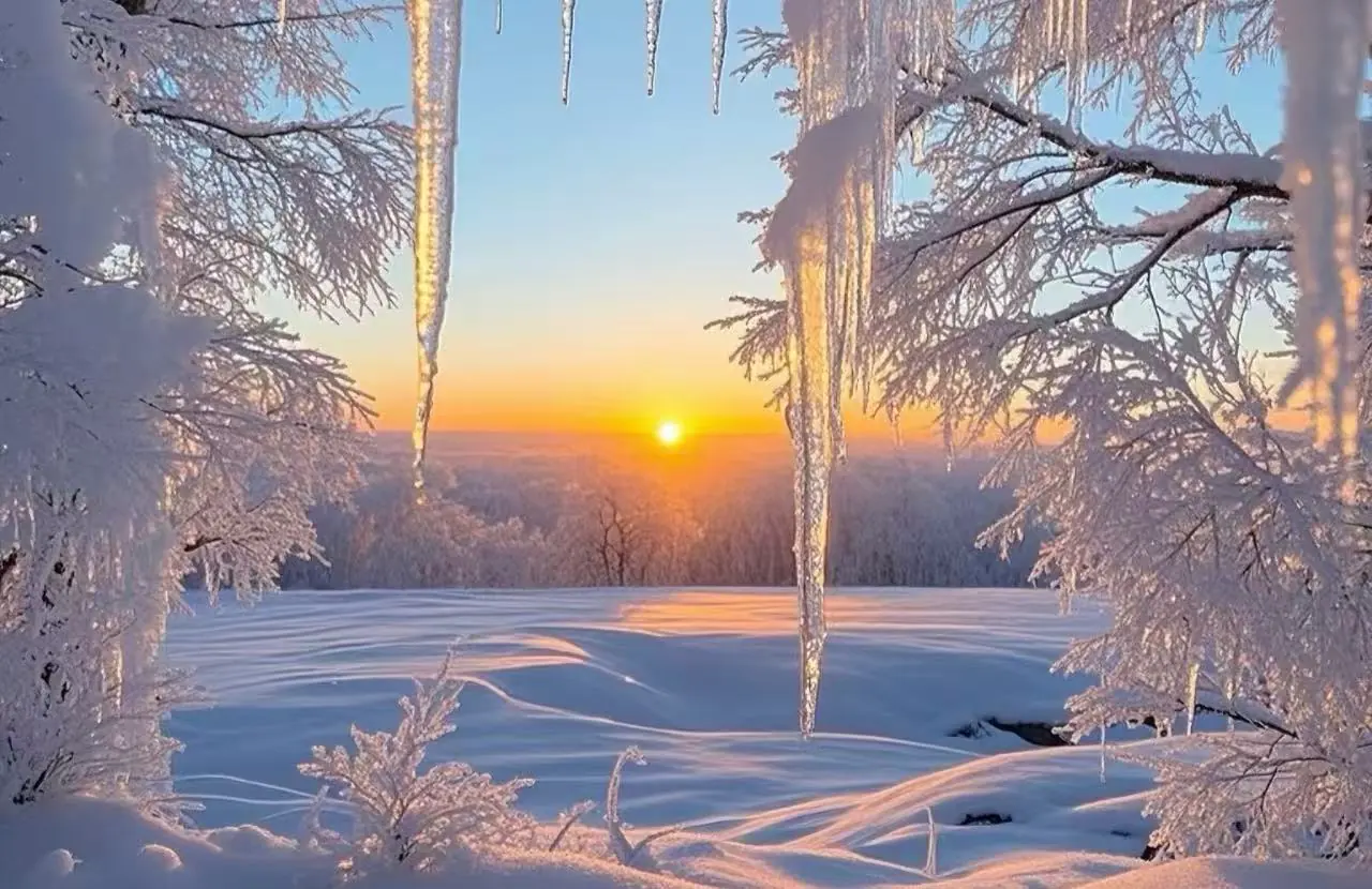 Snowy winter landscape at sunset with icicles hanging from frosted branches and a sun on the horizon.