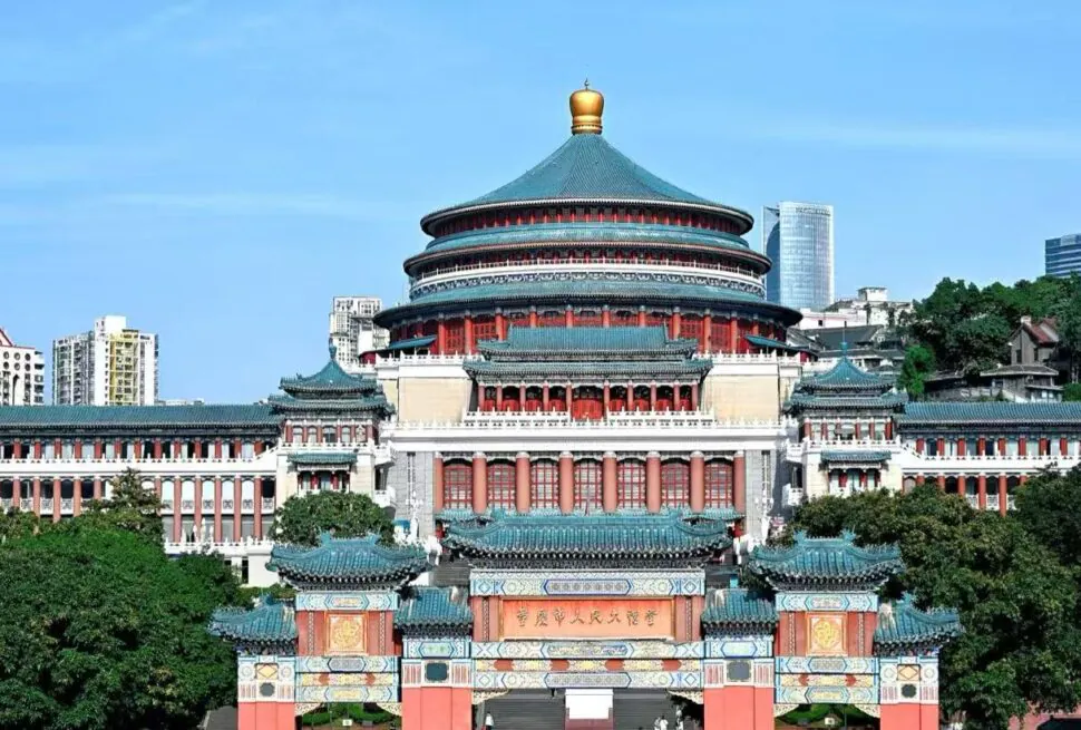 People’s Assembly Hall,Chongqing,Chinatour Large Chinese temple complex with a circular, multi-tiered roofed hall and ornate gate in the foreground, flanked by red columns and turquoise tiles against a city skyline.