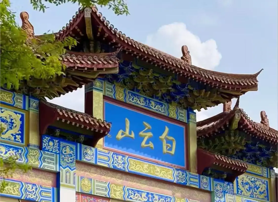 Ornate Chinese temple gate with a blue plaque bearing gold Chinese characters and decorative blue-yellow patterns under a tiled red roof.