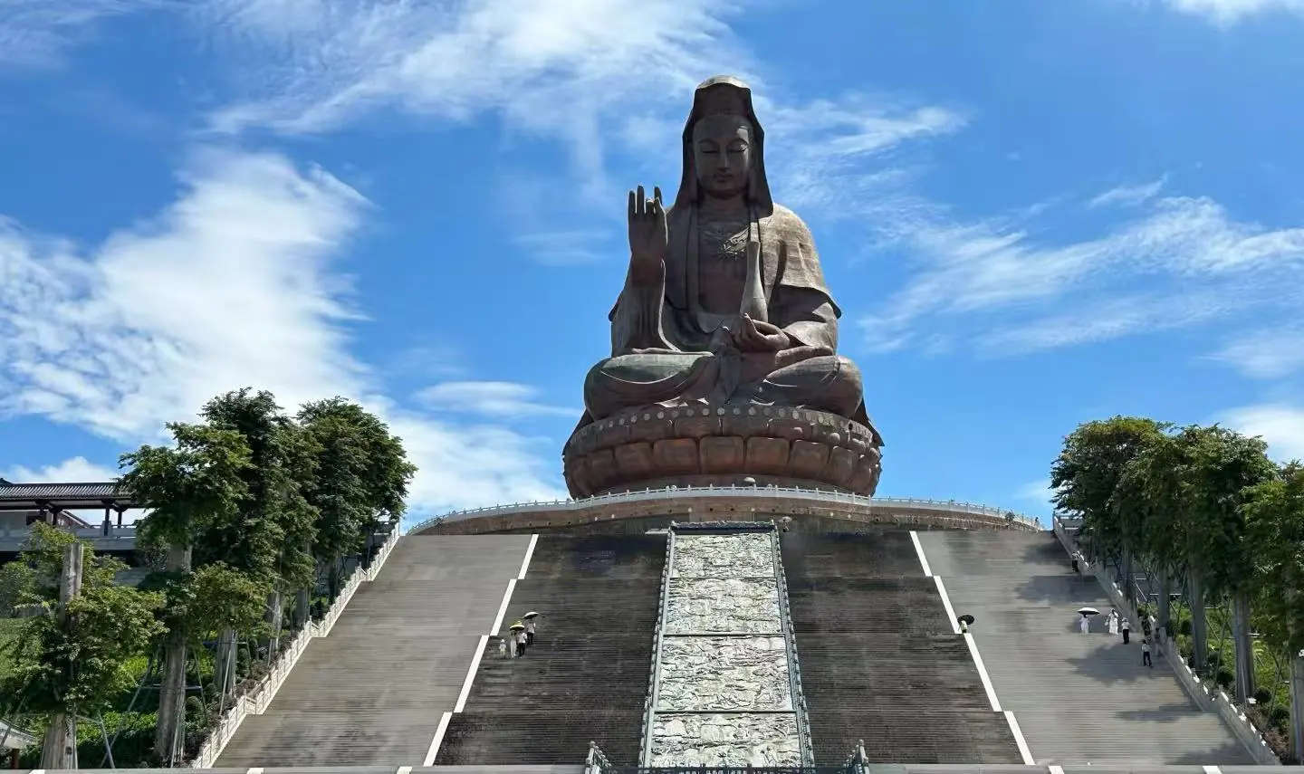 Xiqiao Mountain,Foshan,Chinatour Giant seated statue of Guanyin atop a wide stone staircase under a blue sky.