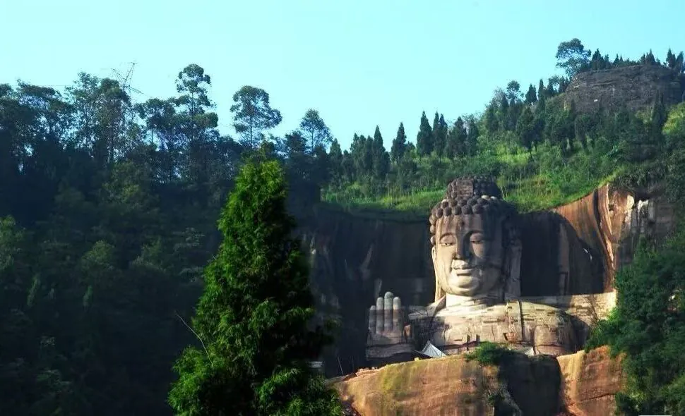 Large carved Buddha statue in a cliff face, with right hand raised in blessing, surrounded by trees.