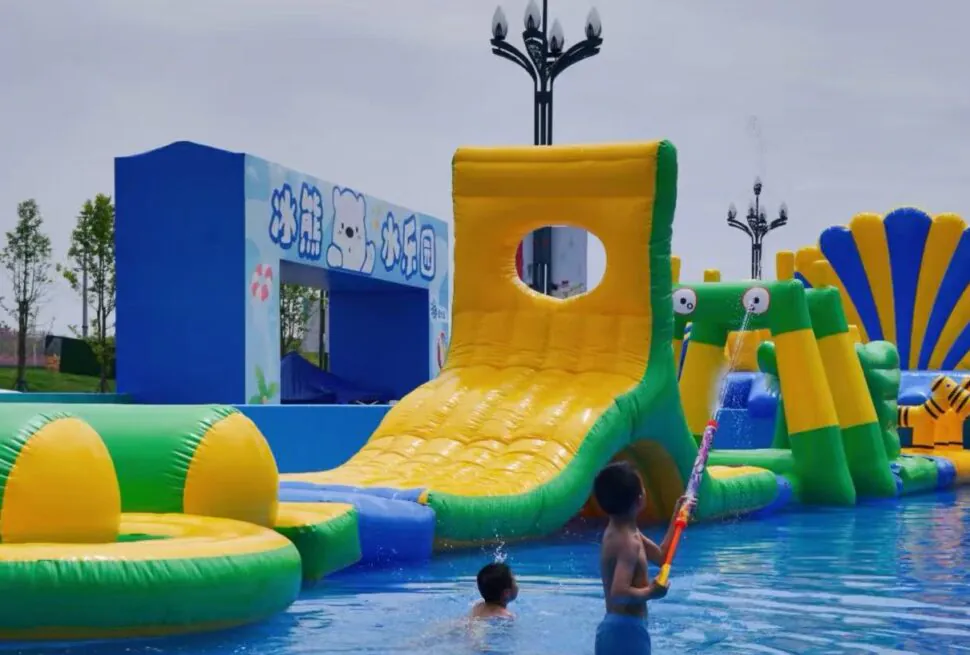 Colorful inflatable water park with a large yellow slide, green and blue obstacles, and children playing in a pool.