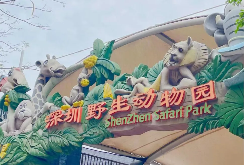 Shenzhen Safari Park,Shenzhen,Chinatour Entrance arch of Shenzhen Safari Park with colorful animal sculptures and tropical foliage (giraffe, monkey, birds) above the sign in Chinese characters and English text.