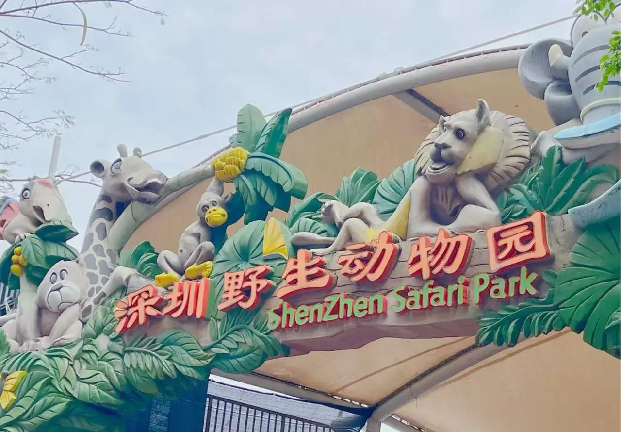 Shenzhen Safari Park,Shenzhen,Chinatour Entrance arch of Shenzhen Safari Park with colorful animal sculptures and tropical foliage (giraffe, monkey, birds) above the sign in Chinese characters and English text.