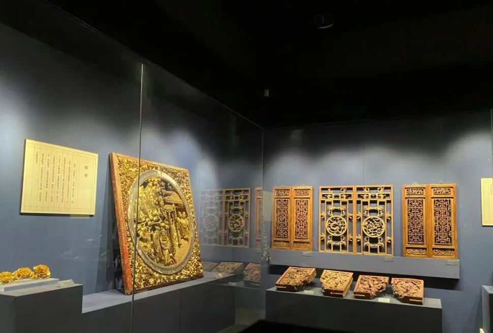 Wenzhou Museum ,Wenzhou,Chinatour Ornate gilded wooden panels and carved plaques on display in a museum case against a dark wall.