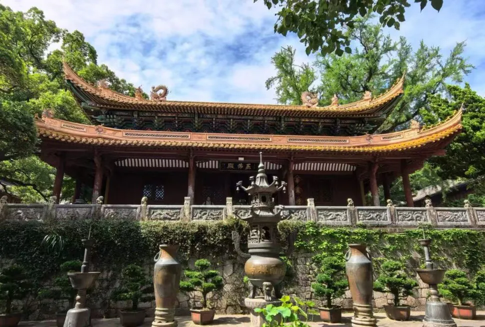 Fayu Temple,Zhoushan,Chinatour Traditional Chinese temple with a curved, ornate roof, stone railing, and surrounding trees in a tranquil courtyard.