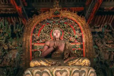Seated Buddha statue in a temple with an ornate gilded backdrop and lotus throne.