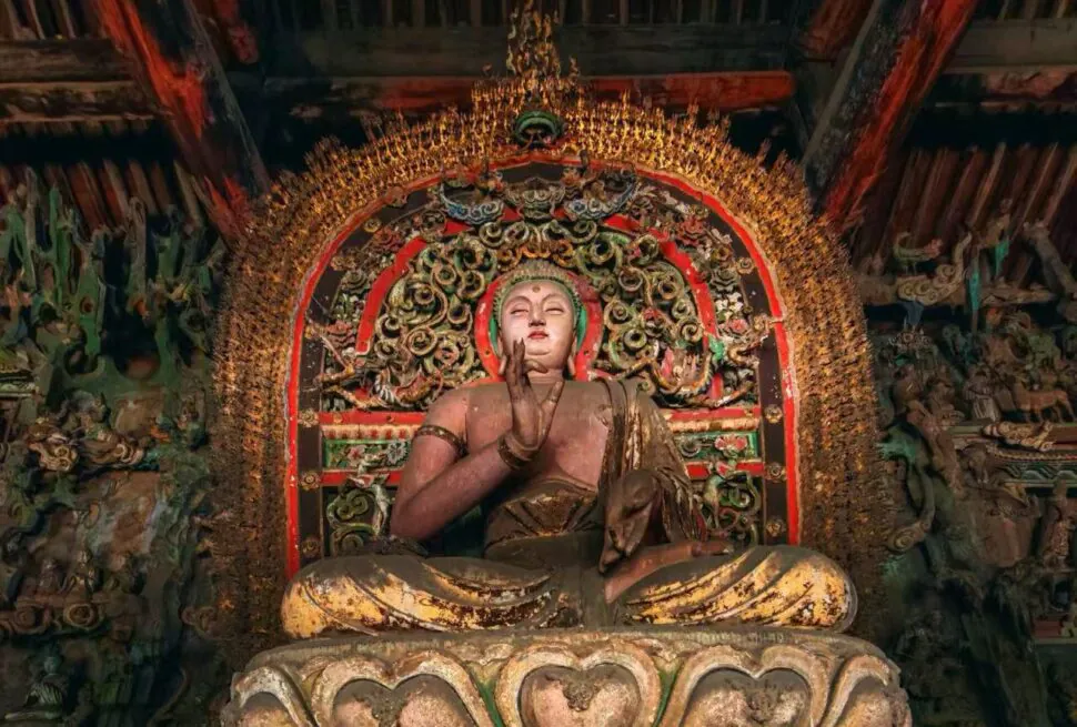 Pingyao Shuanglin Temple,Pingyao,Chinatour Seated Buddha statue in a temple with an ornate gilded backdrop and lotus throne.