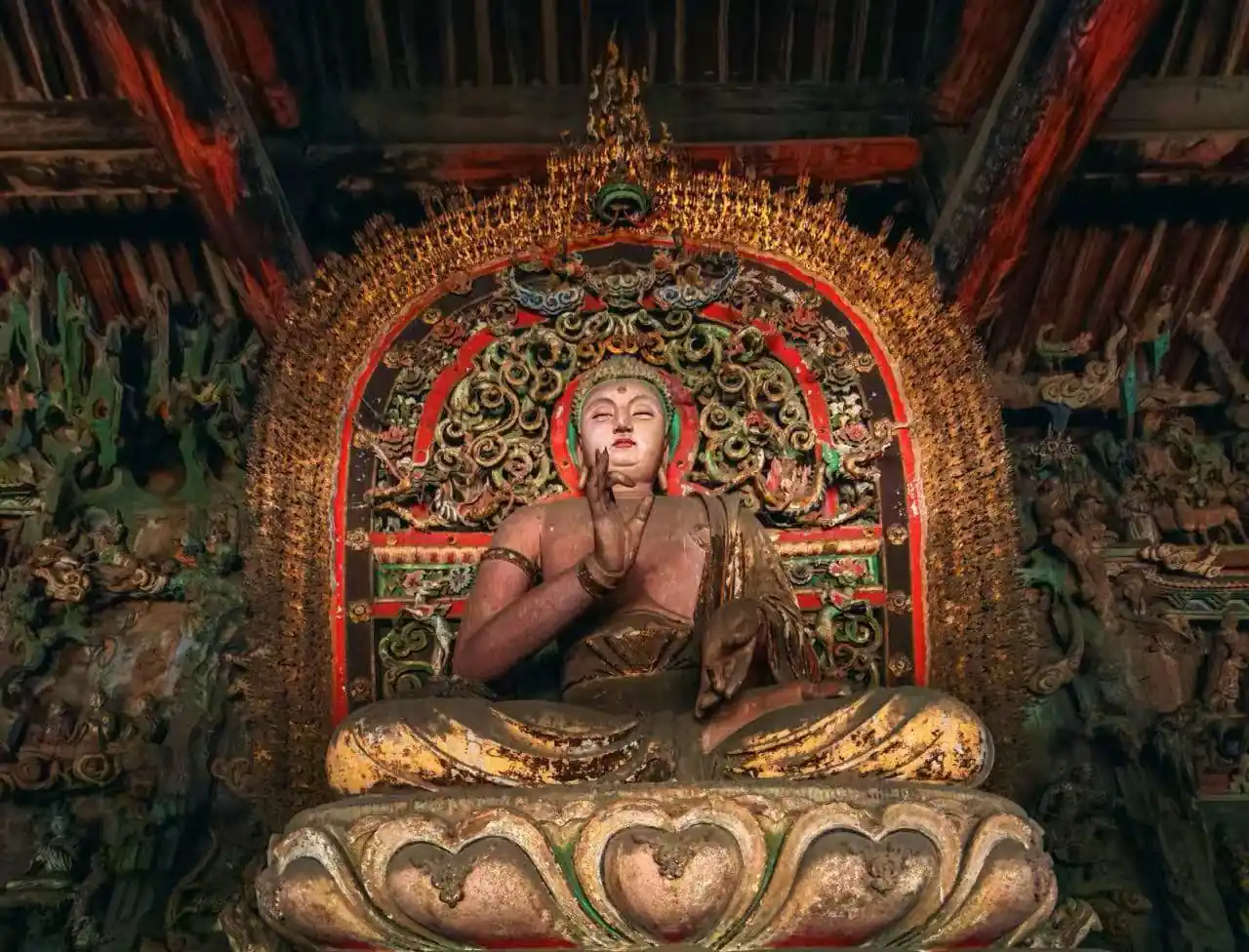 Pingyao Shuanglin Temple,Pingyao,Chinatour Seated Buddha statue in a temple with an ornate gilded backdrop and lotus throne.