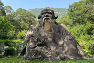 Mount Qingyuan Scenic Area,Quanzhou,Chinatour Large stone statue of a seated ancient sage with a long beard in a lush garden/park setting.