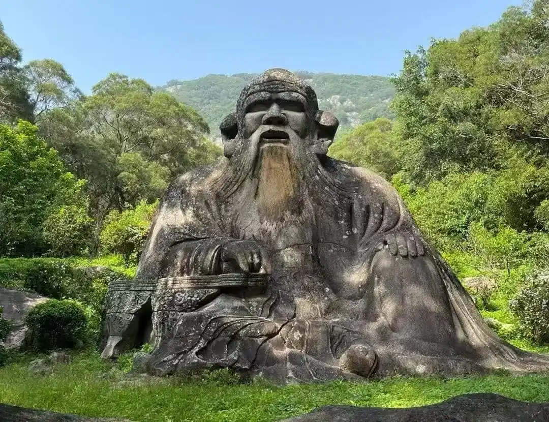 Mount Qingyuan Scenic Area,Quanzhou,Chinatour Large stone statue of a seated ancient sage with a long beard in a lush garden/park setting.