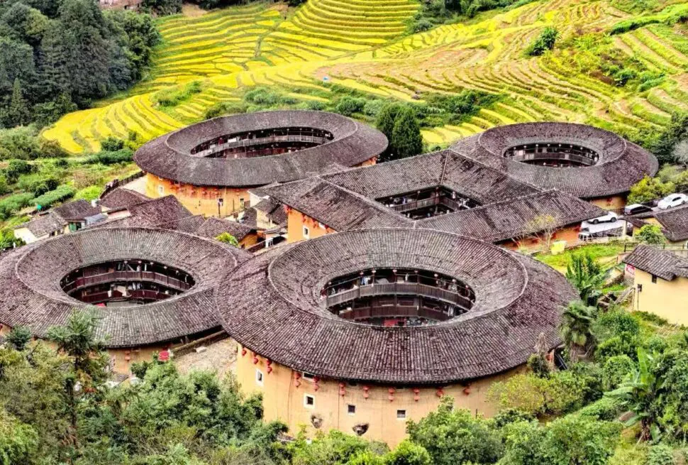 Tianluokeng Tulou Cluster,Zhangzhou,Chinatour Cluster of round tulou earth buildings with inner courtyards in a hillside village; terraced fields in the background, lush greenery surrounding.