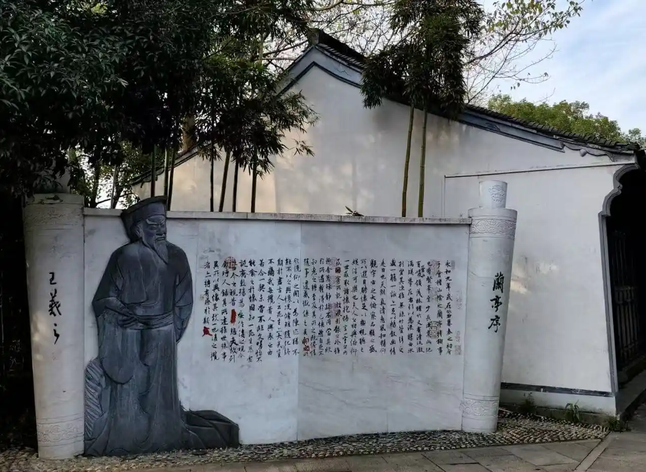 Hometown of the Sage of Calligraphy ,Shaoxing,Chinatour Carved stone relief of a seated scholar beside a wall with Chinese calligraphy and columns in a garden setting.