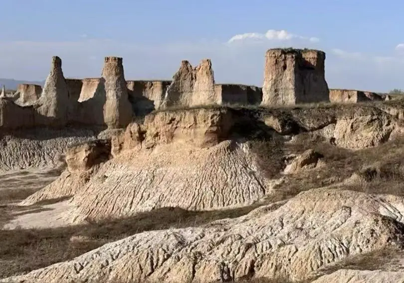 Desert badlands with tall eroded buttes and jagged ridges under a clear blue sky