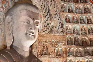 Yungang Grottoes,Datong,Chinatour Giant carved Buddha statue inside a cave temple, with hundreds of smaller Buddha figures in niches along the wall.