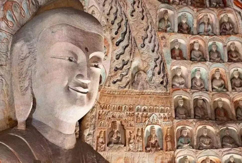 Giant carved Buddha statue inside a cave temple, with hundreds of smaller Buddha figures in niches along the wall.