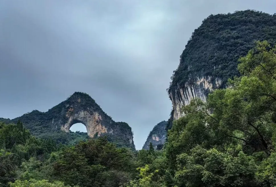 Scenic forested valley with a natural stone arch in the left hill under a cloudy sky.Moon Hill,Yangshuo,Guangxi,Chinatravel