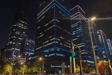 Night city street with sleek glass skyscrapers outlined in blue neon and traffic in the foreground.